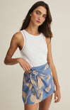 Woman wearing a white sleeveless top and blue floral skirt on a beige background