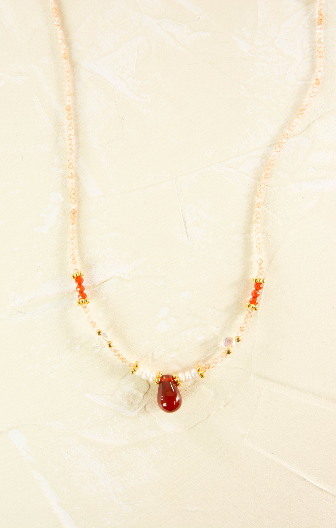 Necklace with red stone and pearls on a beige background