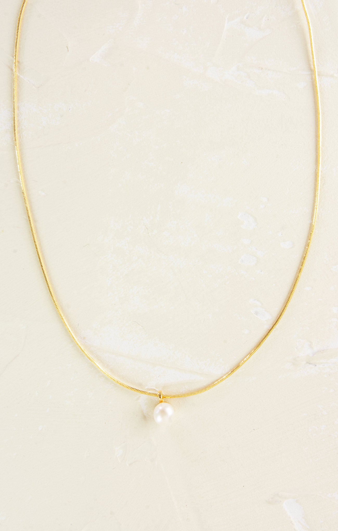 Gold necklace with a single pearl on a light beige background