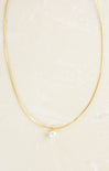 Gold necklace with a single pearl on a light beige background