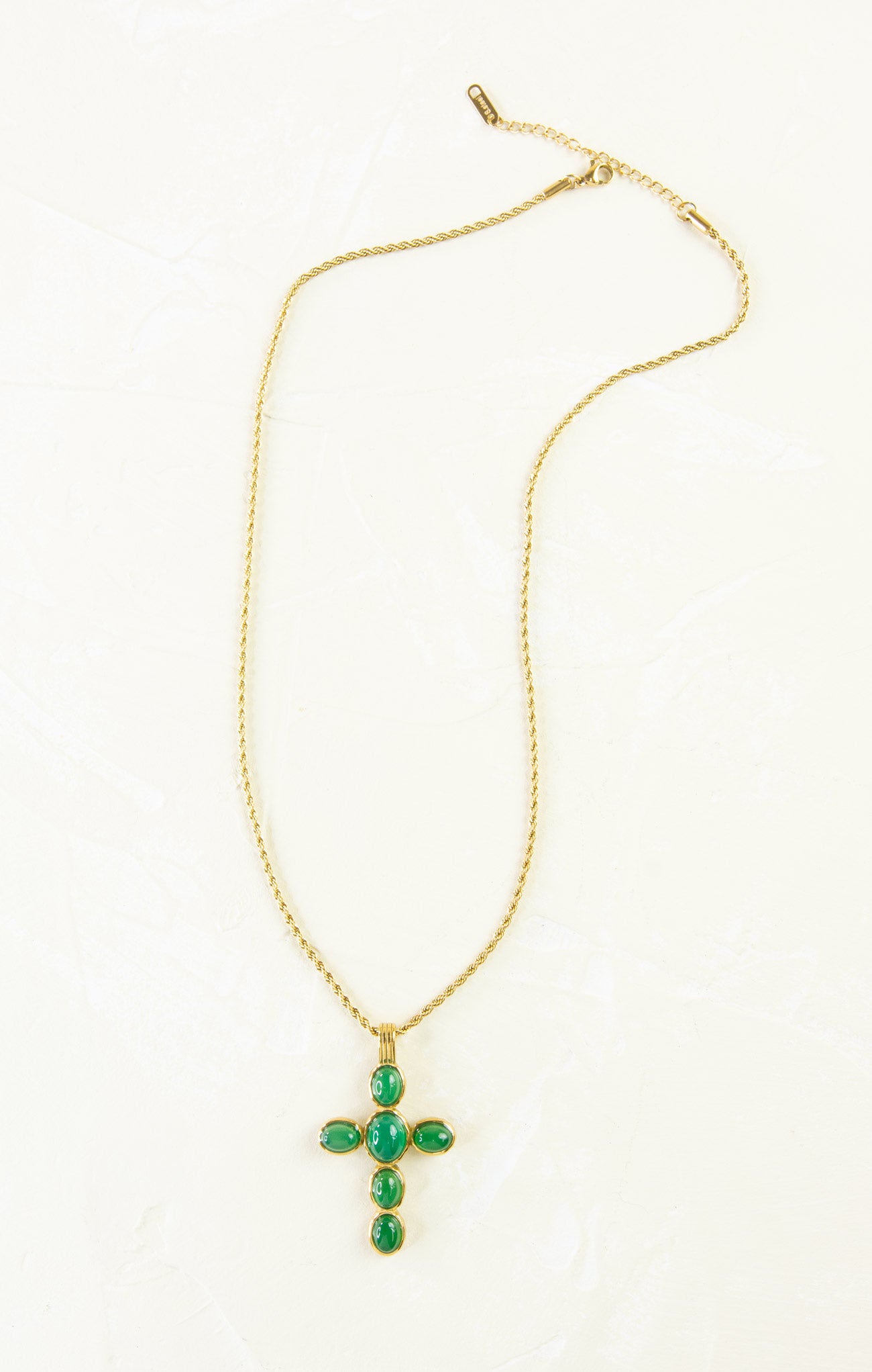 Gold necklace with a green cross pendant on a white background