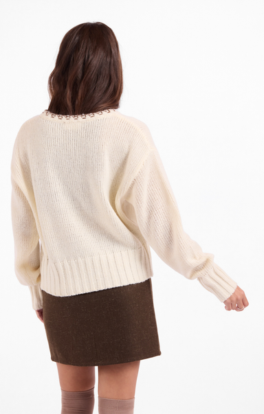 Person wearing a cream sweater with a brown skirt on a white background