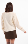 Person wearing a cream sweater with a brown skirt on a white background