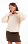 Woman wearing a cream sweater and brown skirt on a white background