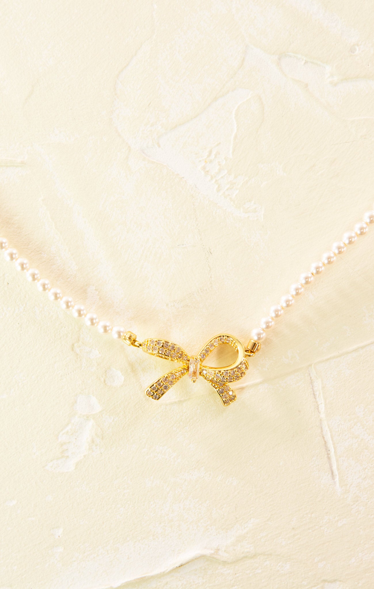 Gold bow-shaped charm on a pearl necklace against a light background