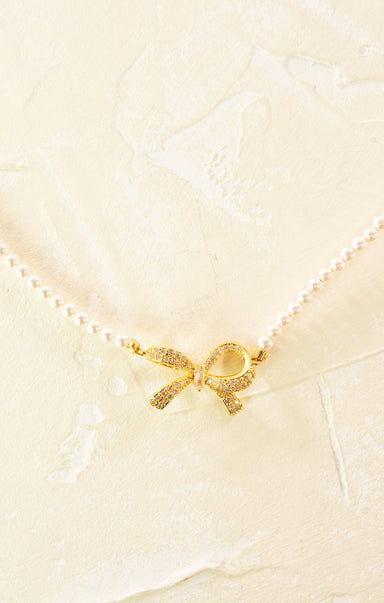 Gold bow-shaped charm on a pearl necklace against a light background