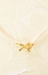 Gold bow-shaped charm on a pearl necklace against a light background