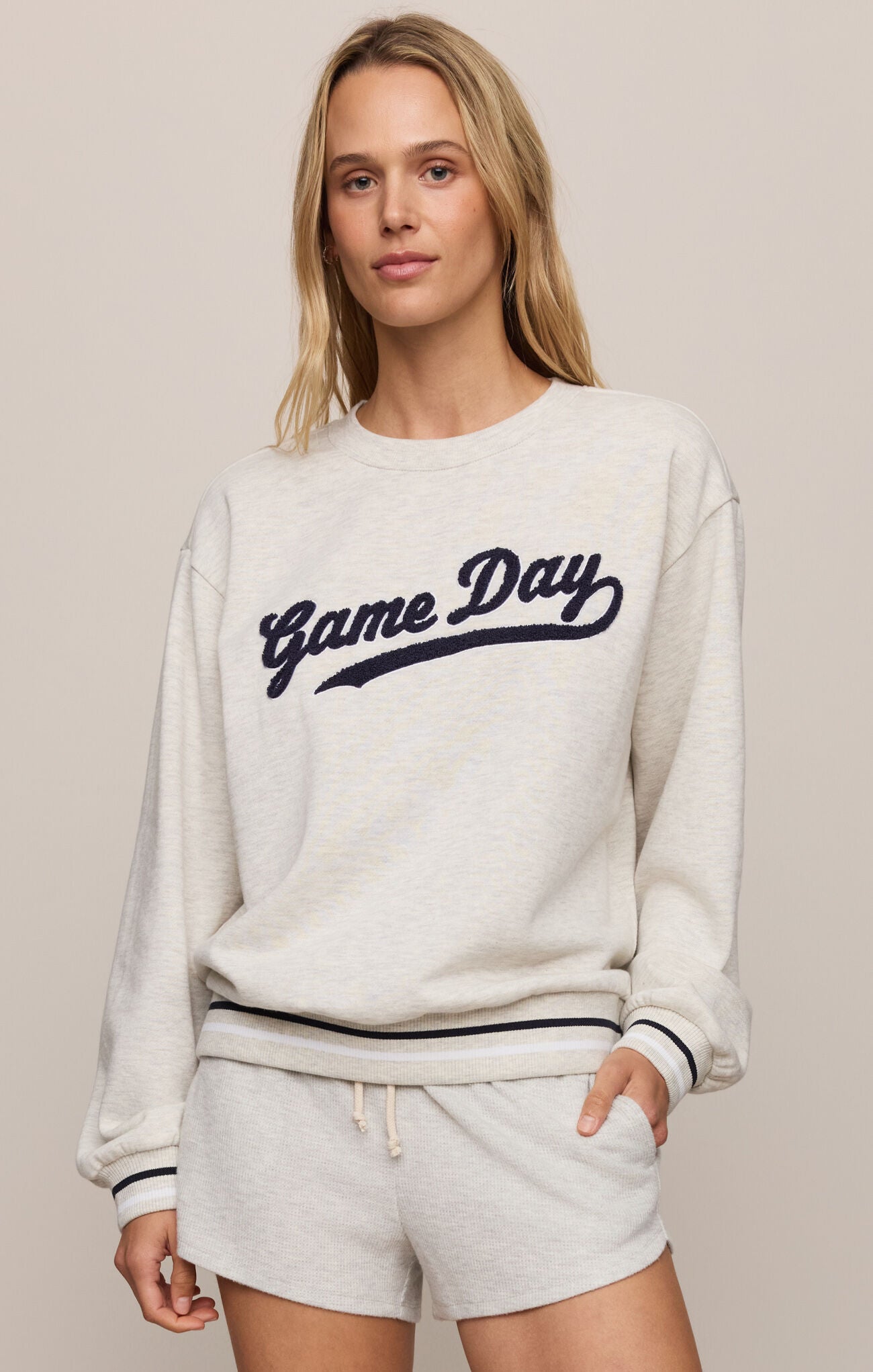 Woman wearing a 'Game Day' sweatshirt and shorts on a beige background