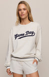 Woman wearing a 'Game Day' sweatshirt and shorts on a beige background
