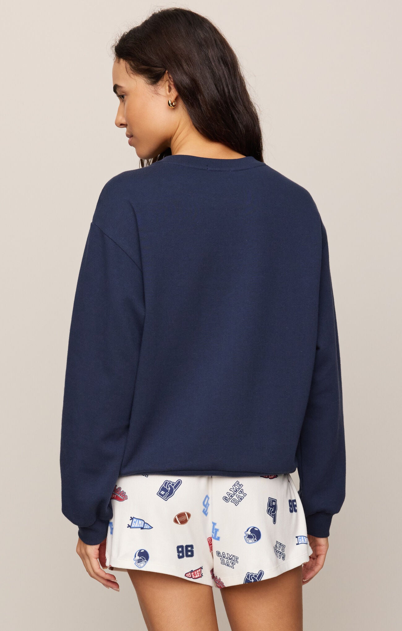 Woman wearing a navy blue sweatshirt and patterned shorts on a beige background