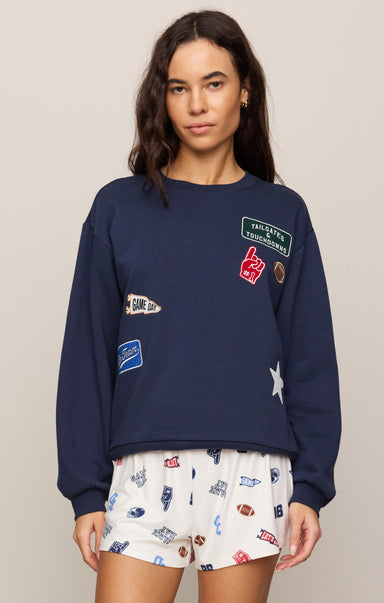 Woman wearing a navy blue sweatshirt with patches and white shorts with sports-themed print on a beige background