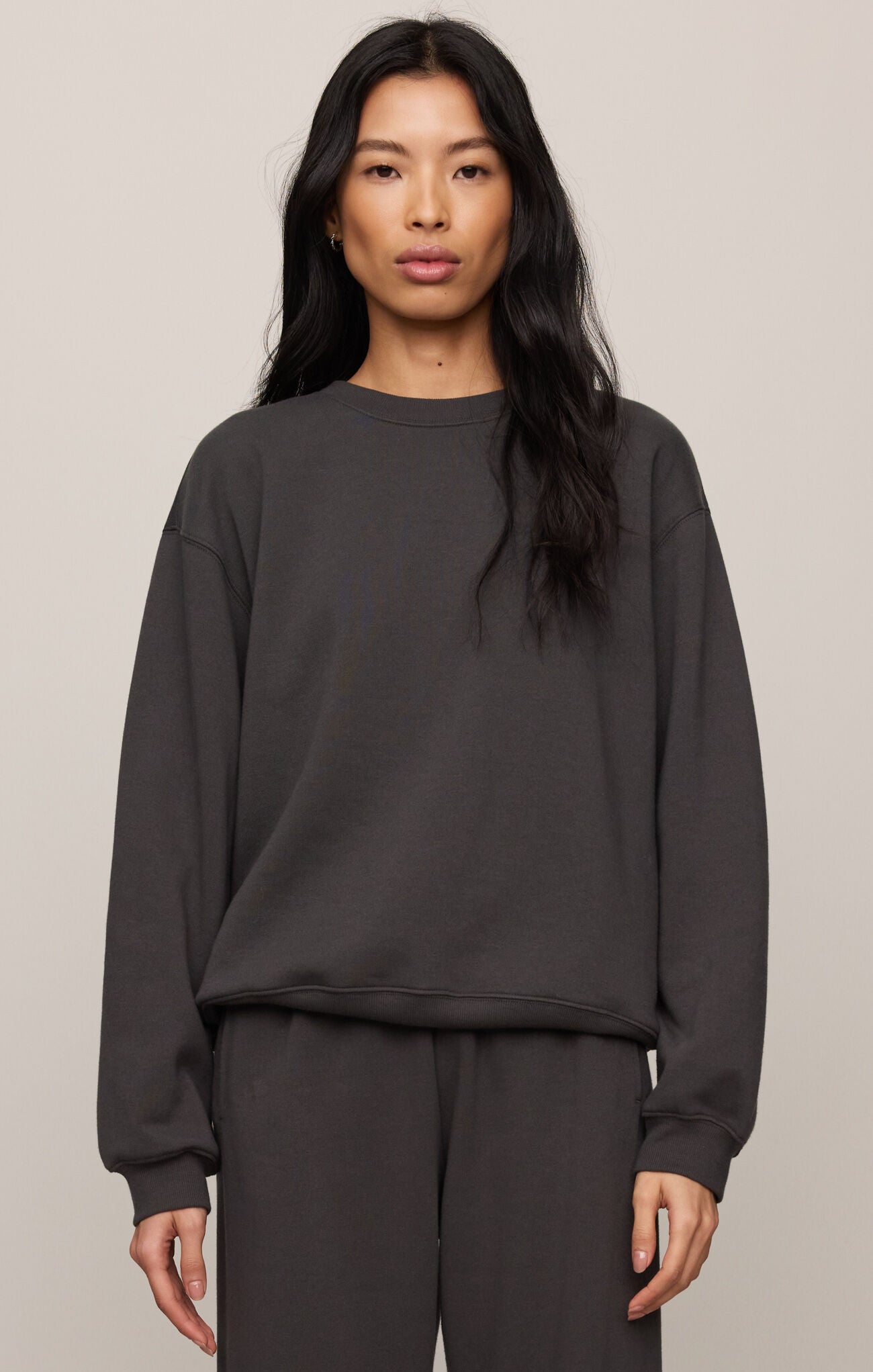 Person wearing a dark gray sweatshirt and pants on a beige background