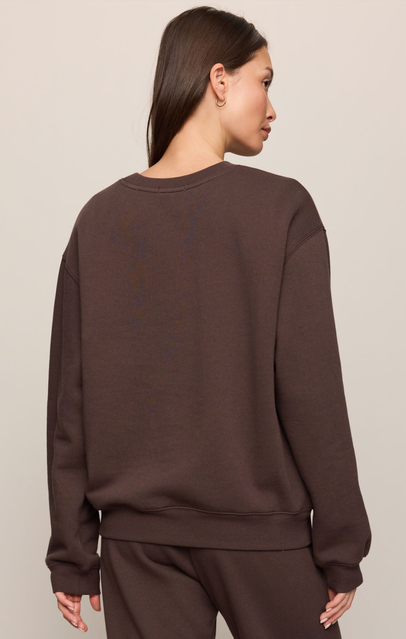 Person wearing a brown sweatshirt and pants on a beige background