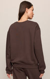 Person wearing a brown sweatshirt and pants on a beige background