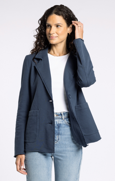 Woman wearing a navy blazer over a white shirt and light blue jeans on a white background