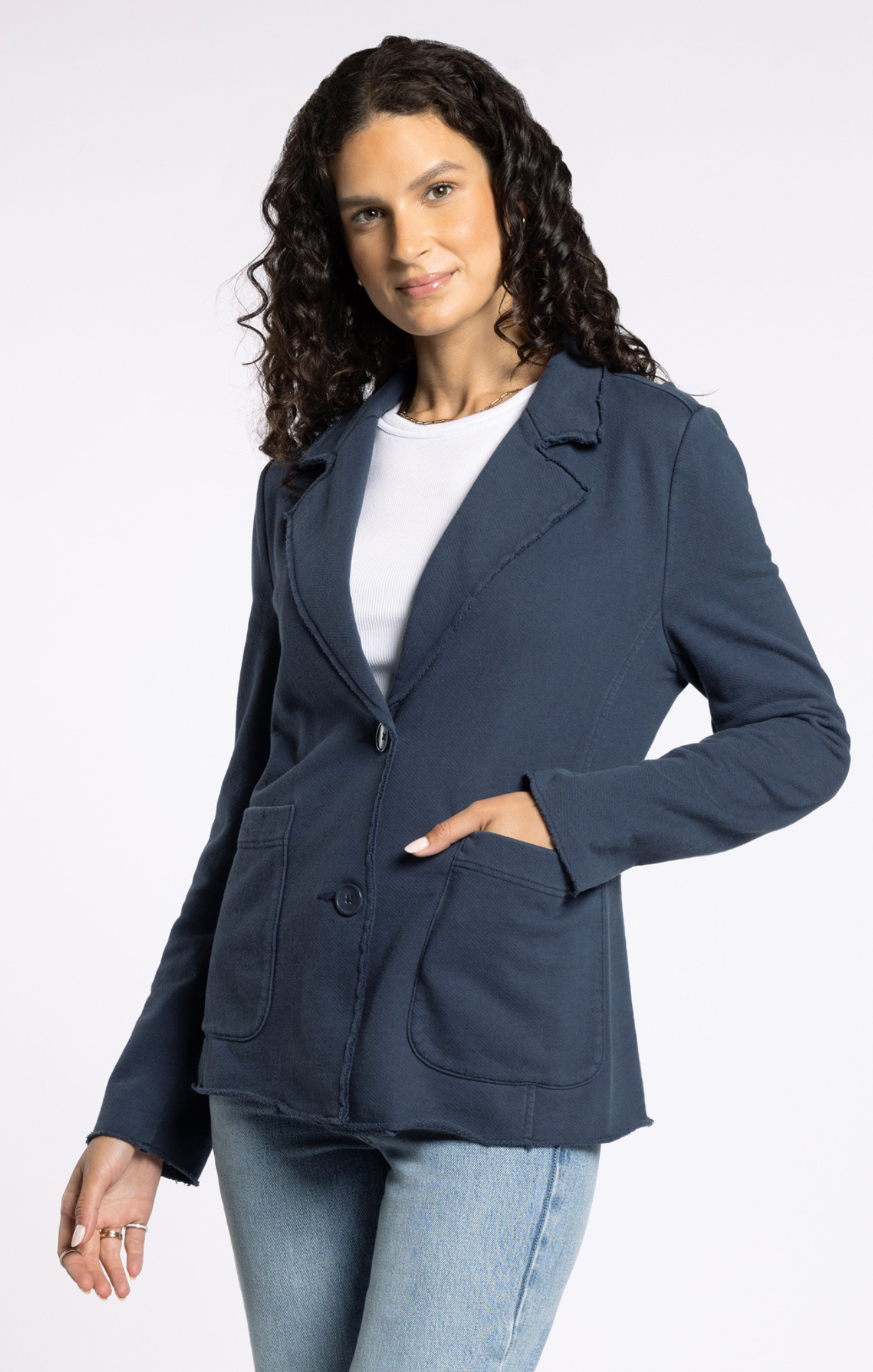 Woman wearing a navy blazer over a white shirt and light blue jeans on a white background