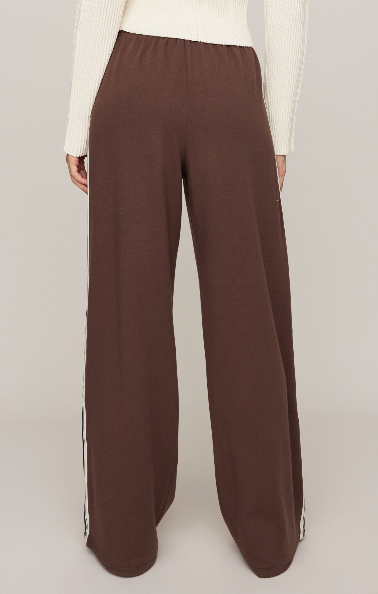 Brown wide-leg pants worn with a white top on a plain background