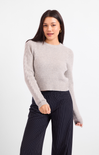 A woman modeling a light gray ribbed knit sweater paired with dark navy pinstriped trousers, shot against a clean white studio background.