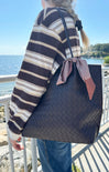 Person holding a black woven handbag with a checkered ribbon by a waterfront