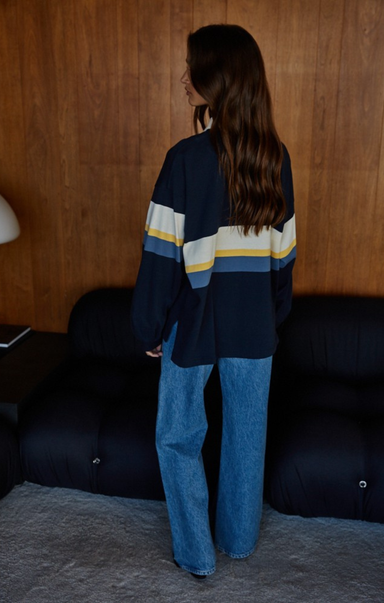 Person wearing a navy sweater with horizontal stripes in a room with wooden walls and a dark sofa.