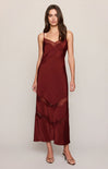A woman modeling a long burgundy satin slip dress with lace trim and spaghetti straps against a plain light gray studio background.