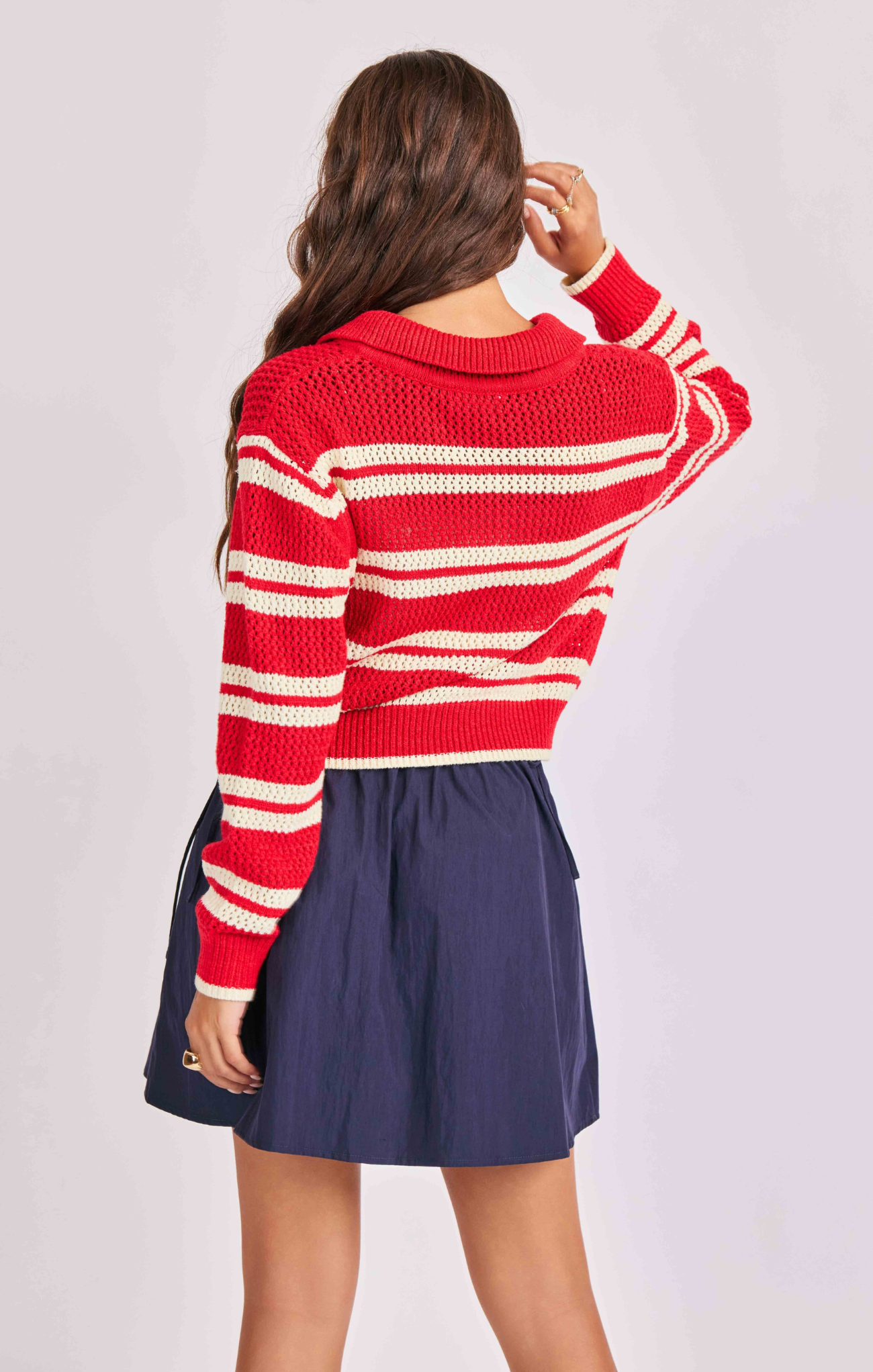 Person wearing a red and white striped sweater and navy skirt on a light gray background