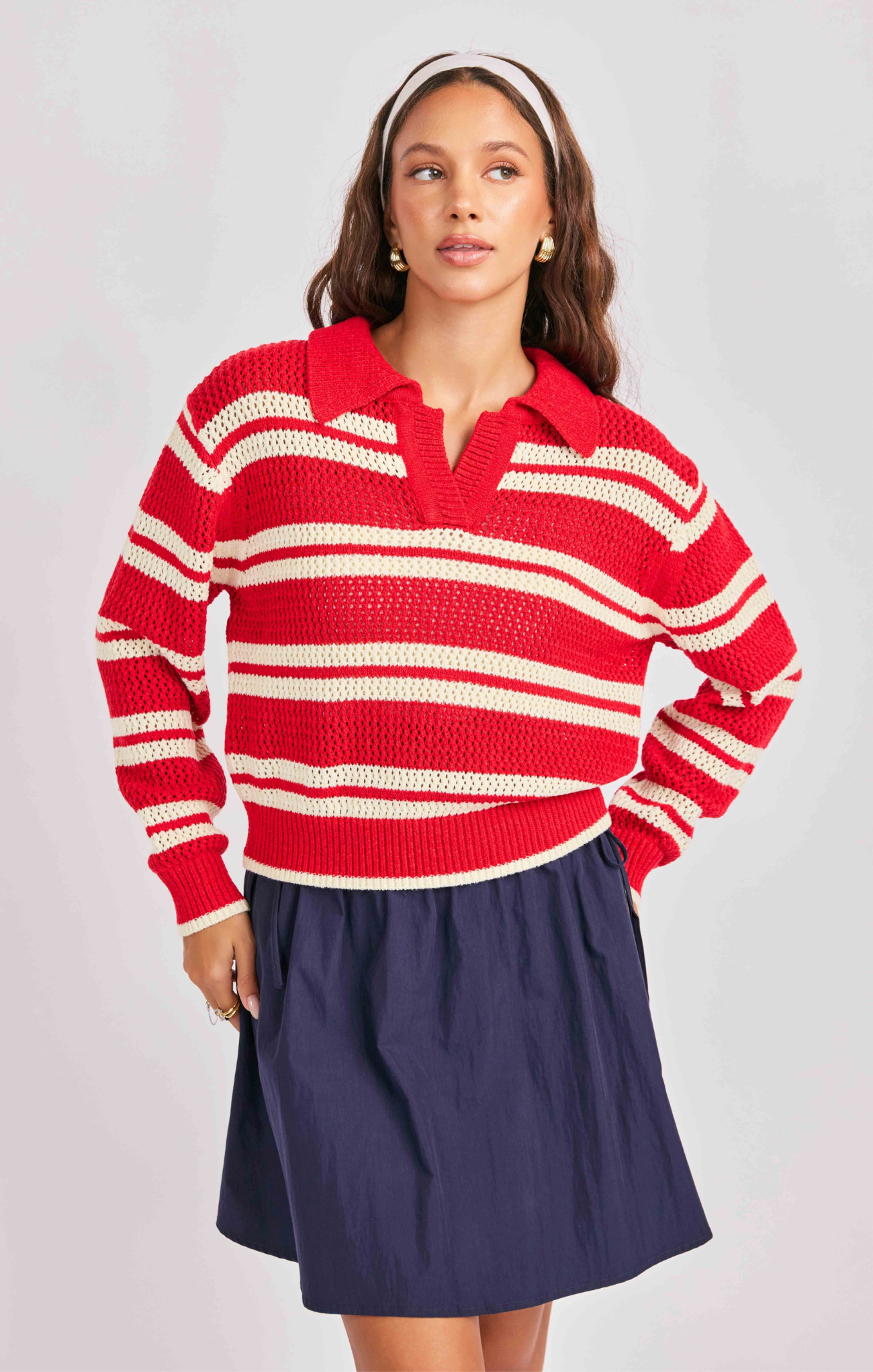 Woman wearing a red and white striped sweater with a navy skirt on a light gray background