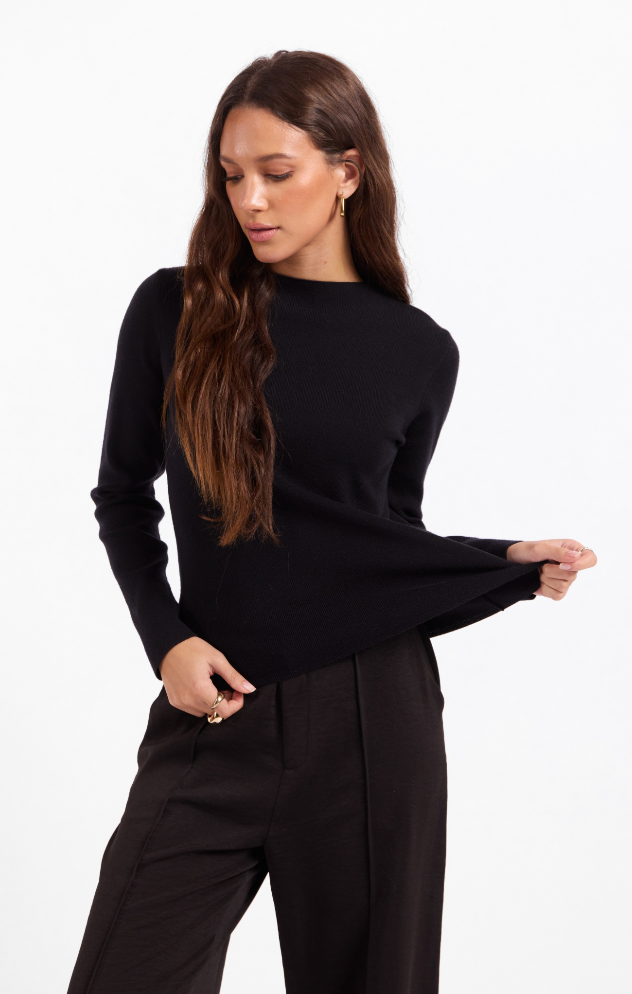 A woman modeling a black long-sleeve knit top and black wide-leg trousers against a plain white studio background.
