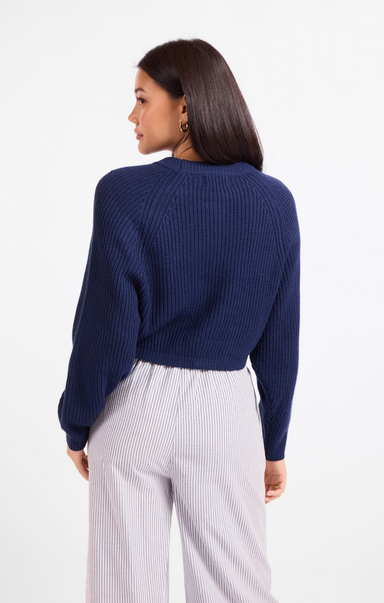 A woman shown from the back wearing a navy blue ribbed knit sweater and light gray pinstriped pants against a plain white studio background.
