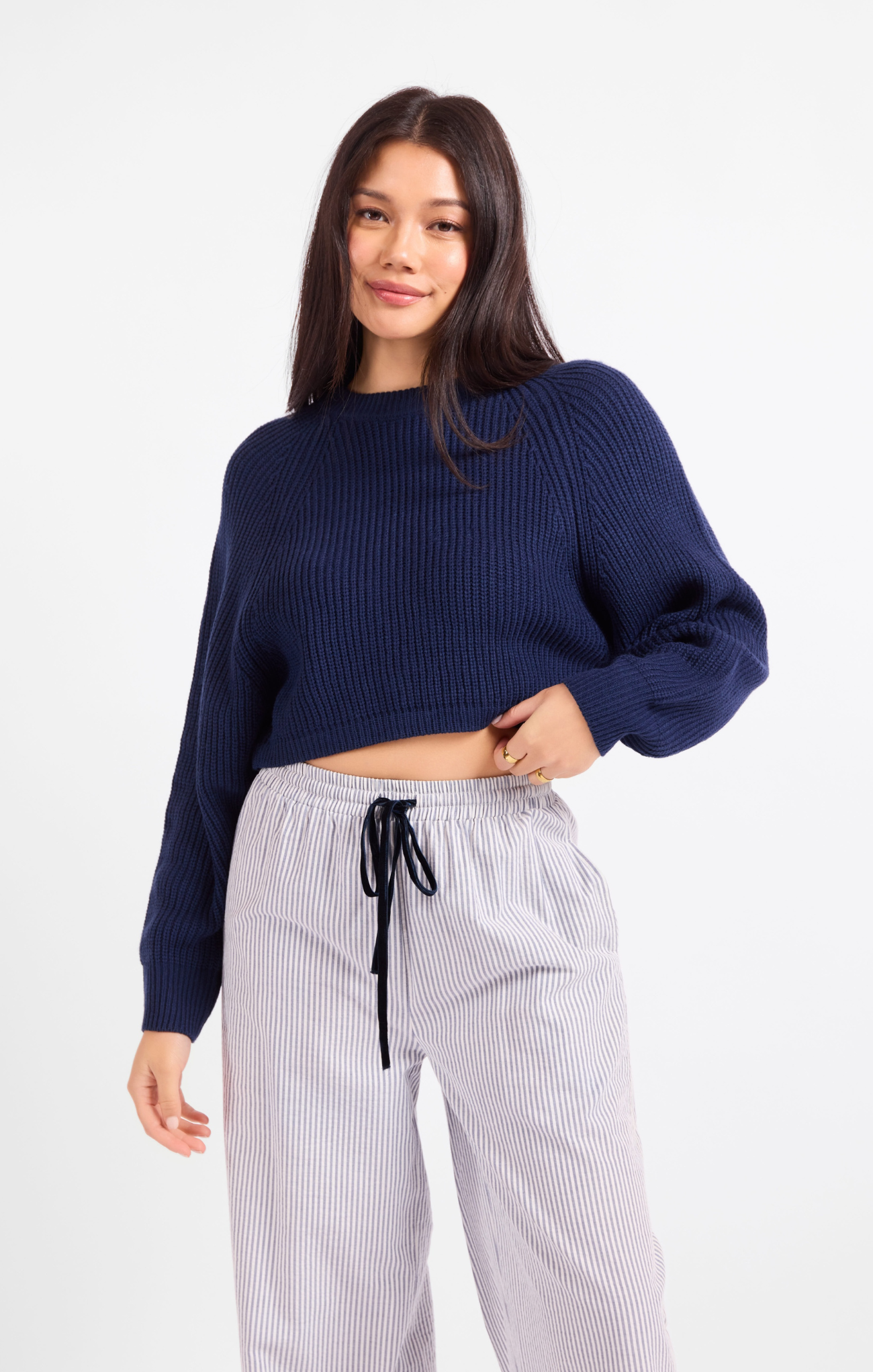 Woman wearing a navy sweater and white striped pants on a white background