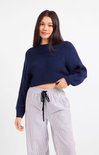 Woman wearing a navy sweater and white striped pants on a white background