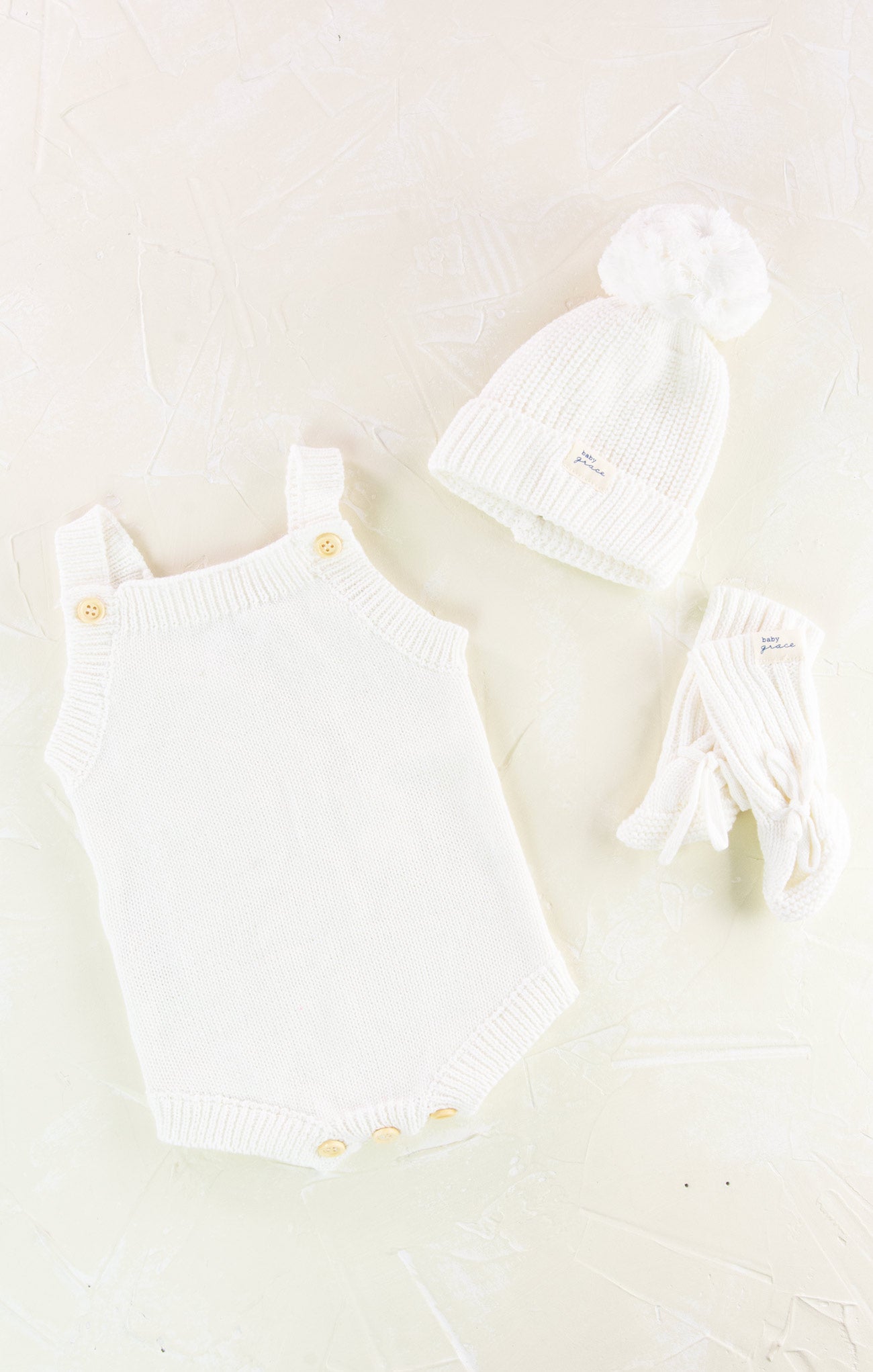White baby romper with yellow buttons and matching hat on a light beige background