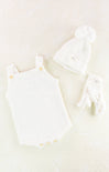 White baby romper with yellow buttons and matching hat on a light beige background