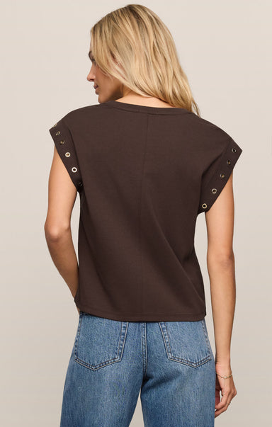 Woman wearing a brown sleeveless top with decorative straps on a beige background