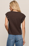 Woman wearing a brown sleeveless top with decorative straps on a beige background