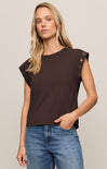 Woman wearing a brown top with unique shoulder designs against a beige background