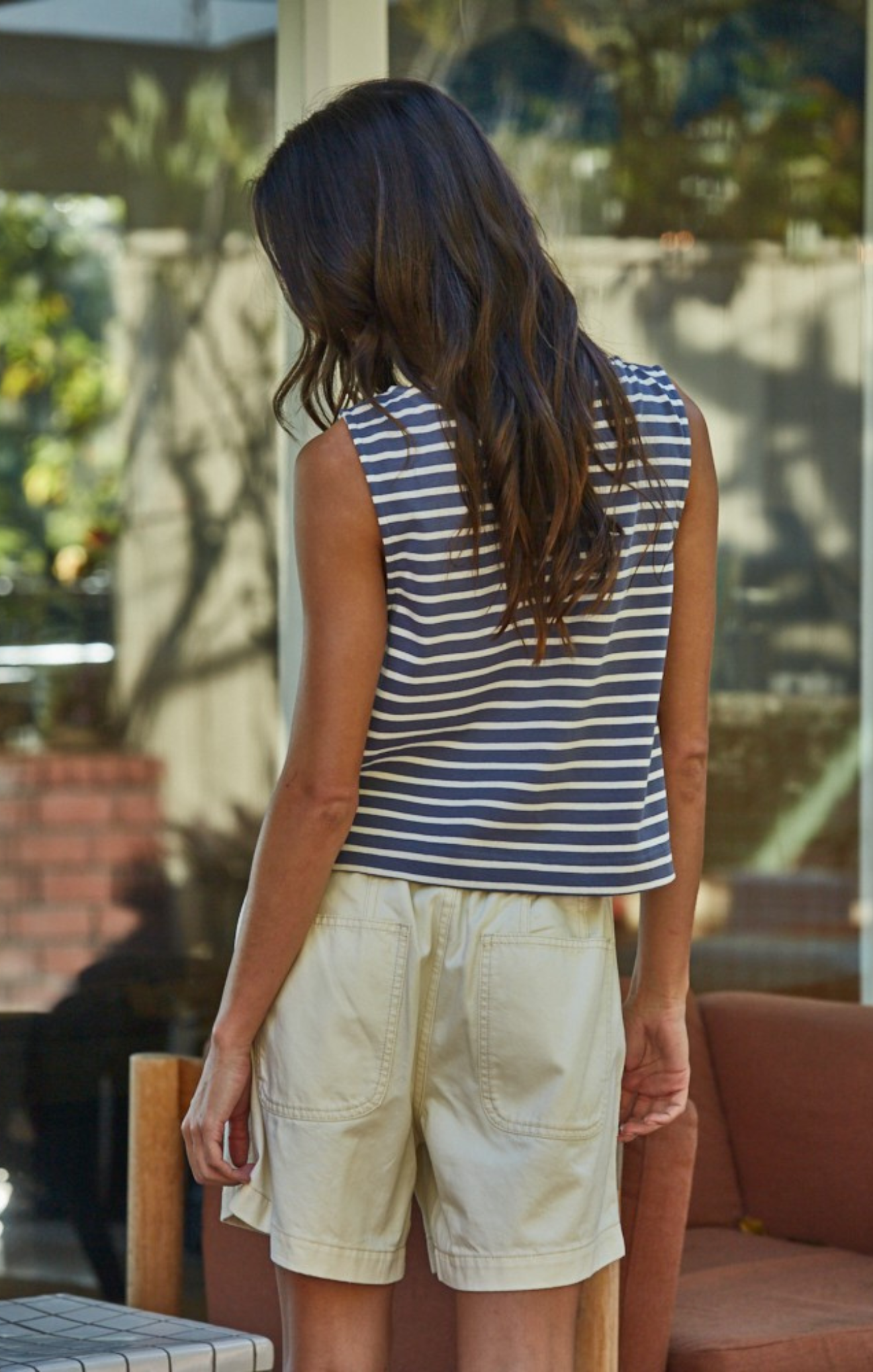 Person wearing a striped sleeveless top and beige shorts standing outdoors.