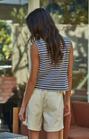 Person wearing a striped sleeveless top and beige shorts standing outdoors.