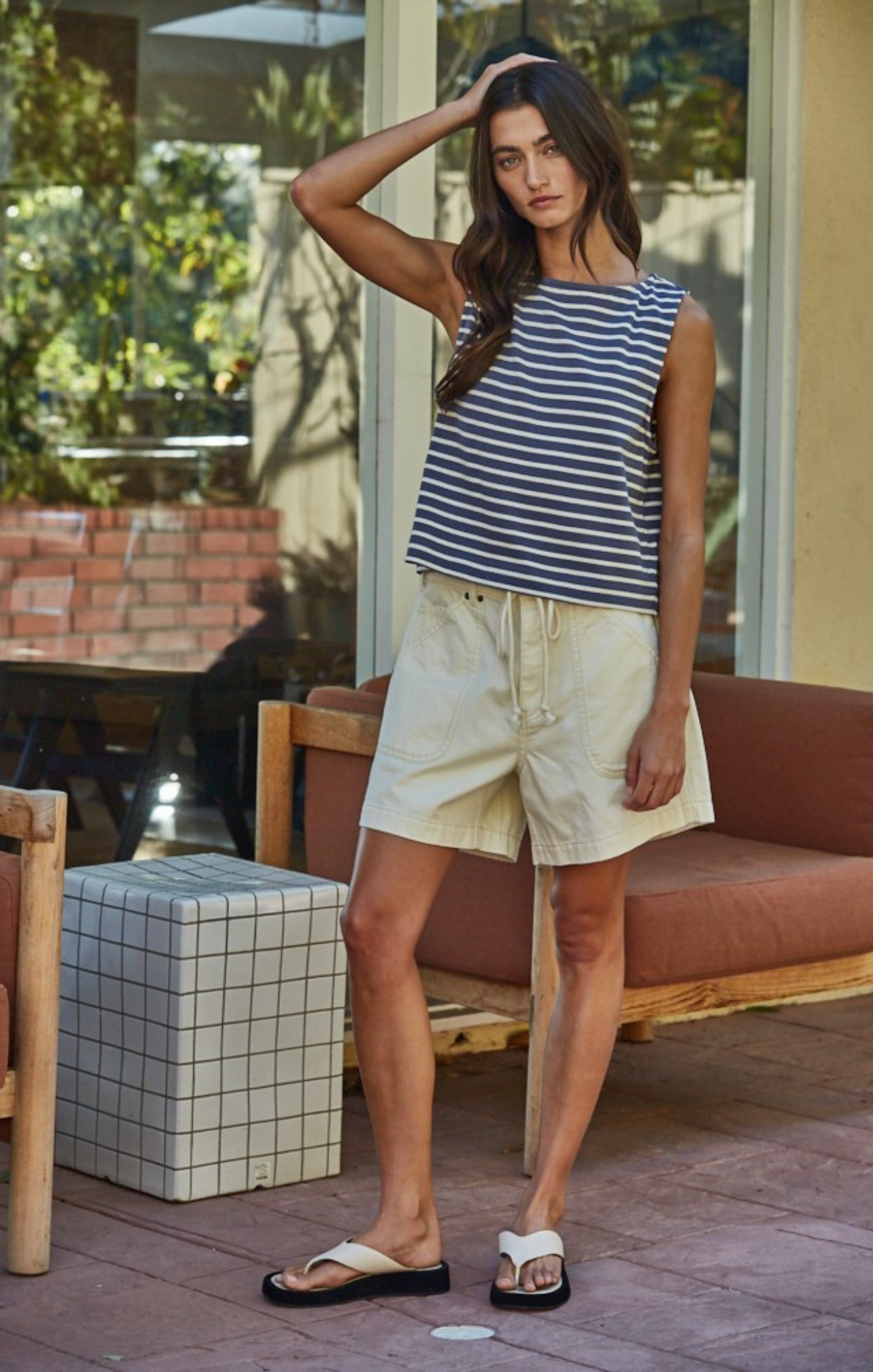 Woman in a striped shirt and shorts standing outdoors on a patio.