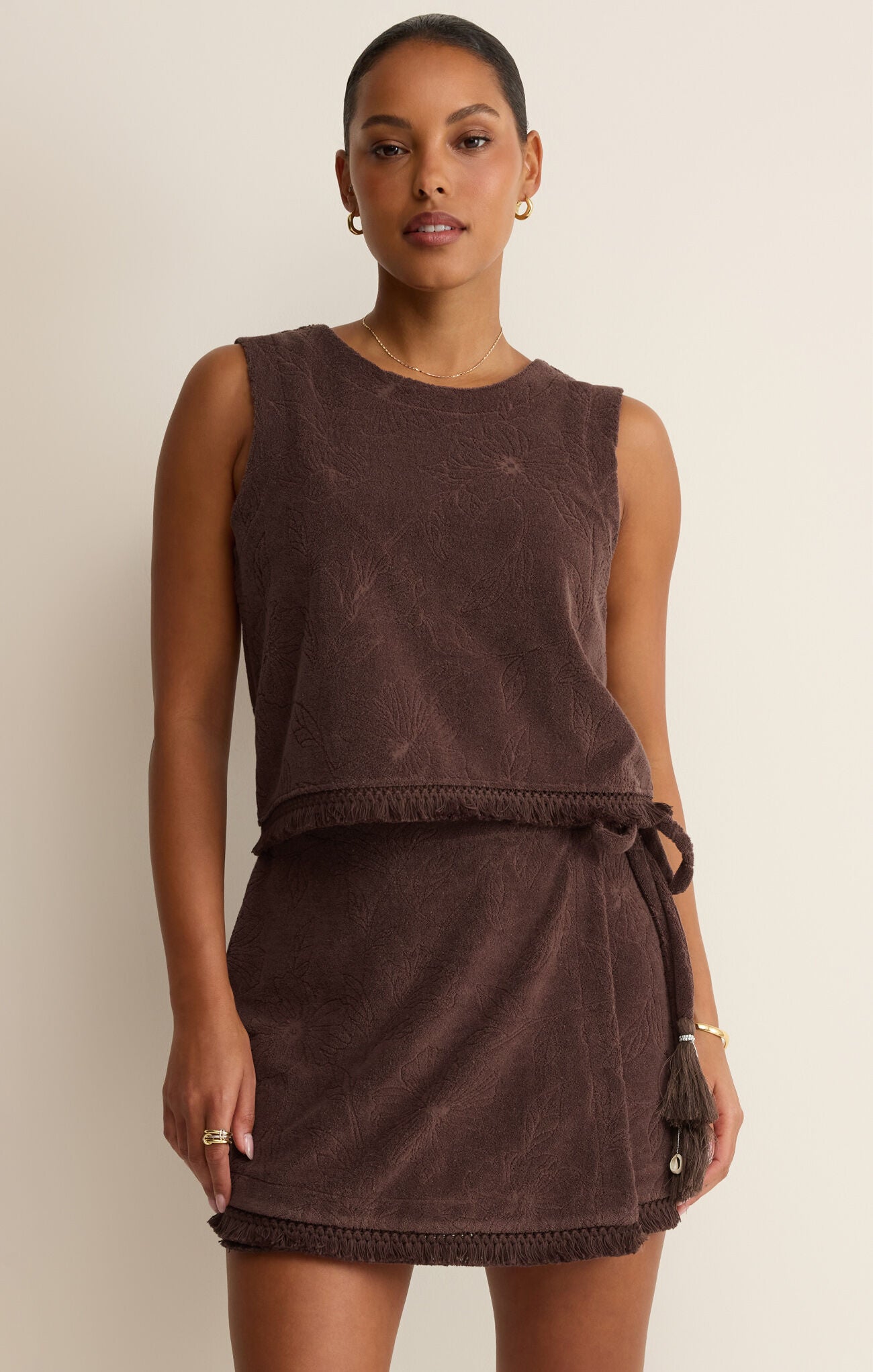 Woman wearing a brown sleeveless dress with a belt against a beige background