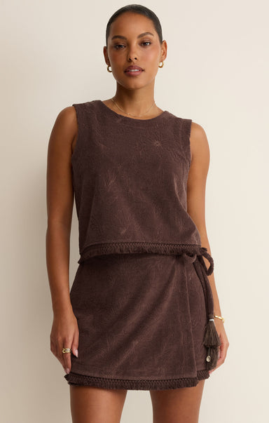Woman wearing a brown sleeveless dress with a belt against a beige background