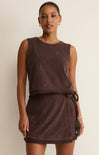 Woman wearing a brown sleeveless dress with a belt against a beige background