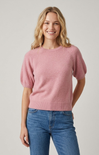 Woman wearing a pink sweater and blue jeans against a plain background