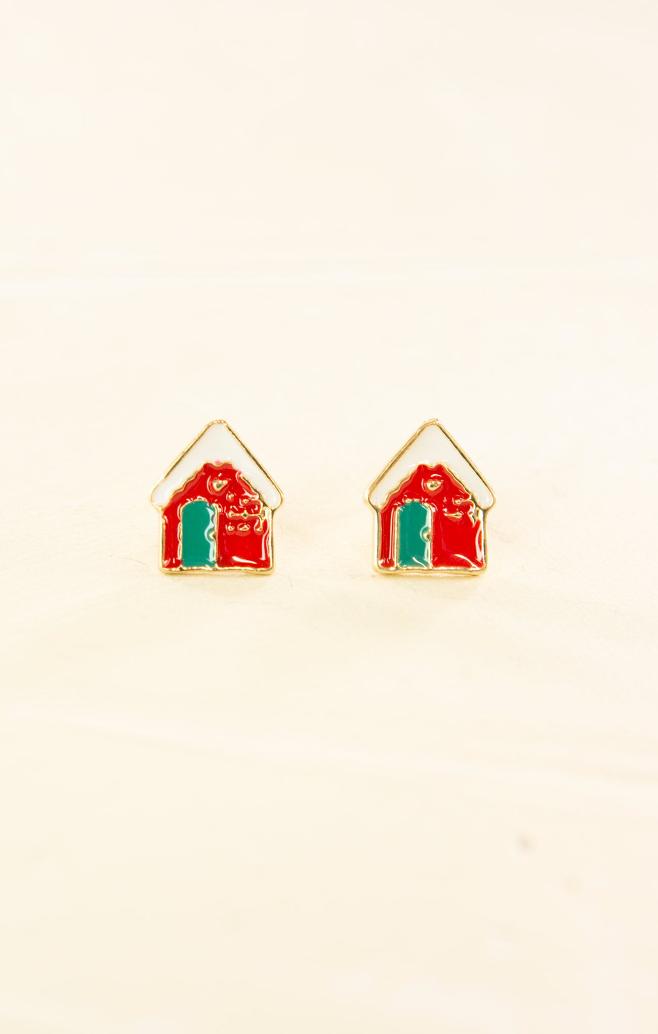 House-shaped earrings with red roofs and green bases on a beige background