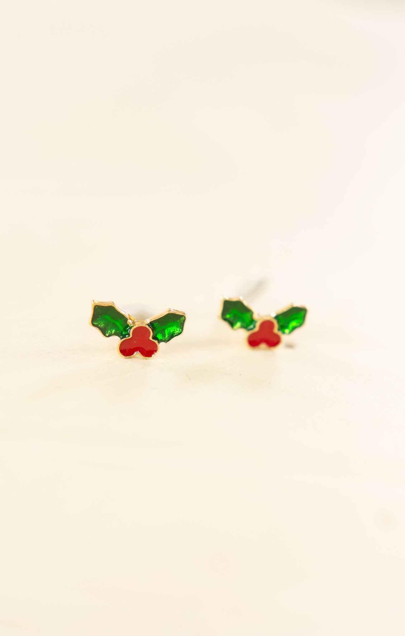 Pair of earrings with green and red designs on a beige background