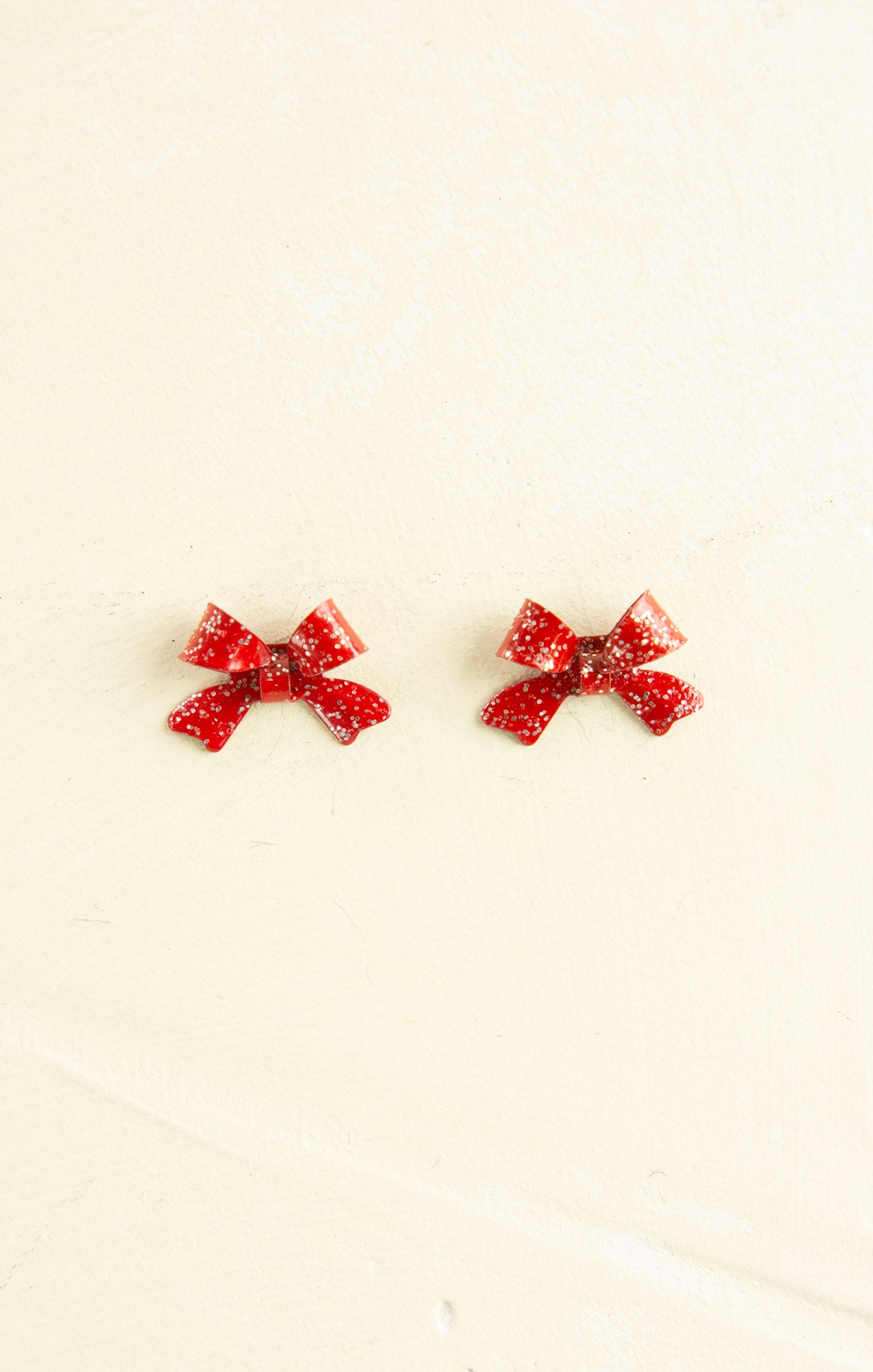 Red bow-shaped earrings on a beige background