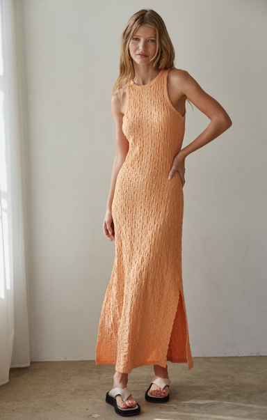 Woman wearing an orange dress standing against a plain wall.