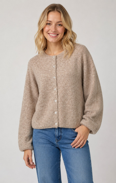 A woman wearing a beige button-front knit cardigan with balloon sleeves and blue jeans, standing against a light gray studio background.