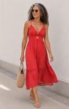 Woman wearing a red dress with a white pattern, holding a woven bag, against a plain background.