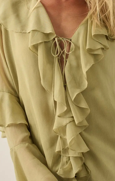 Close-up of a woman wearing a pale sage green blouse with layered ruffles and a tie-front neckline.